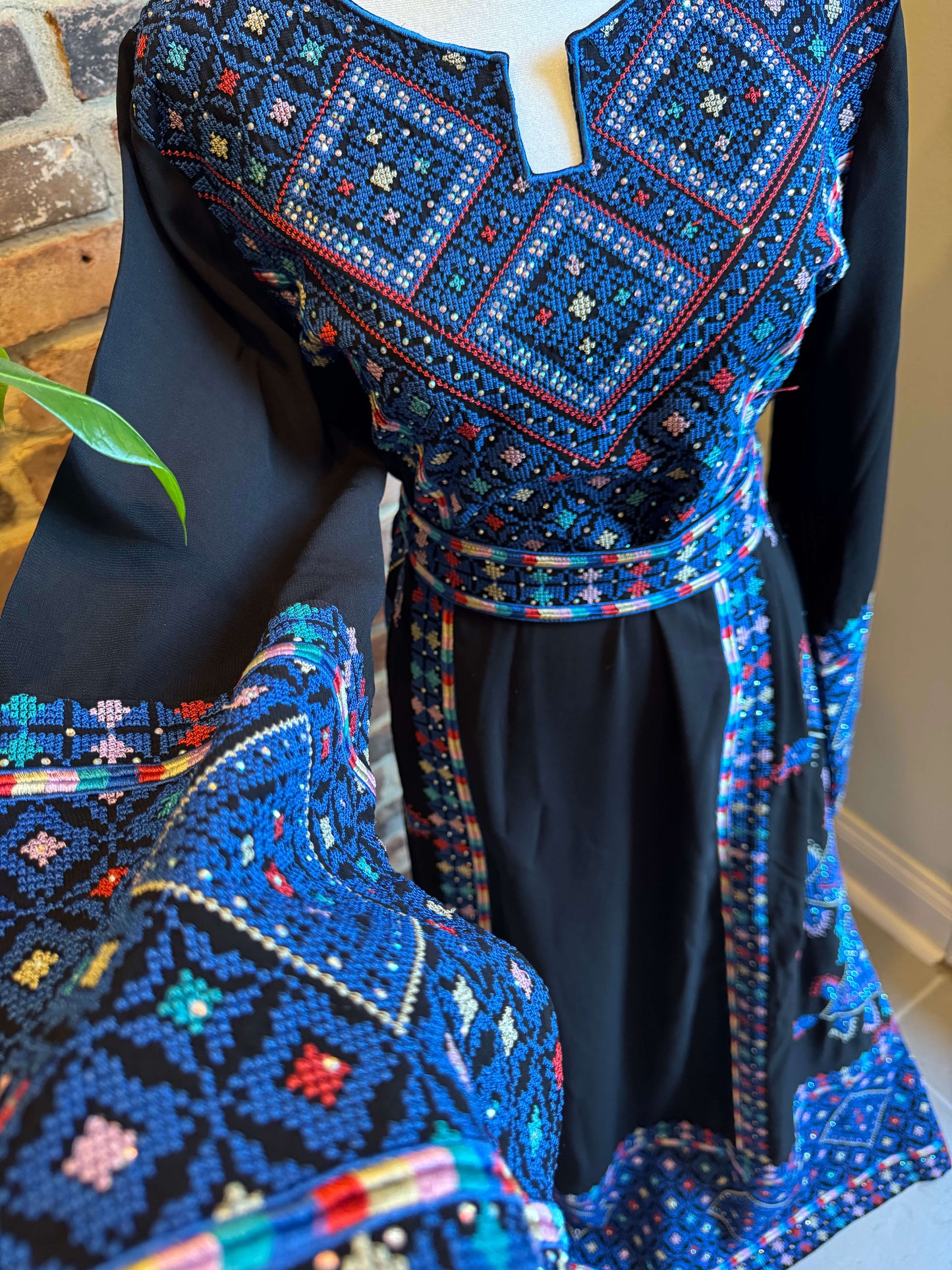 Front view of black Palestinian Ma’inat dress with blue embroidery of sleeve