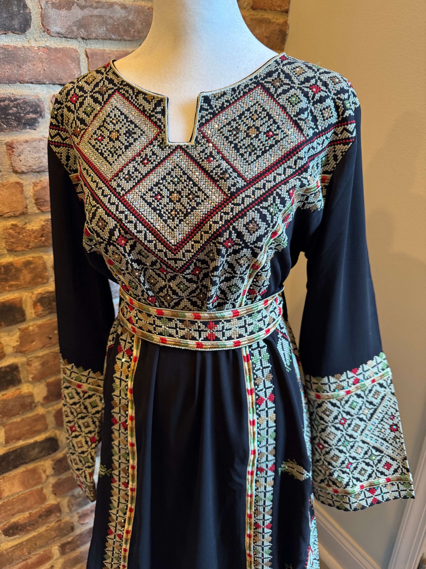 Front view of black Palestinian Ma’inat dress with green/tan embroidery close up of front and sleeve